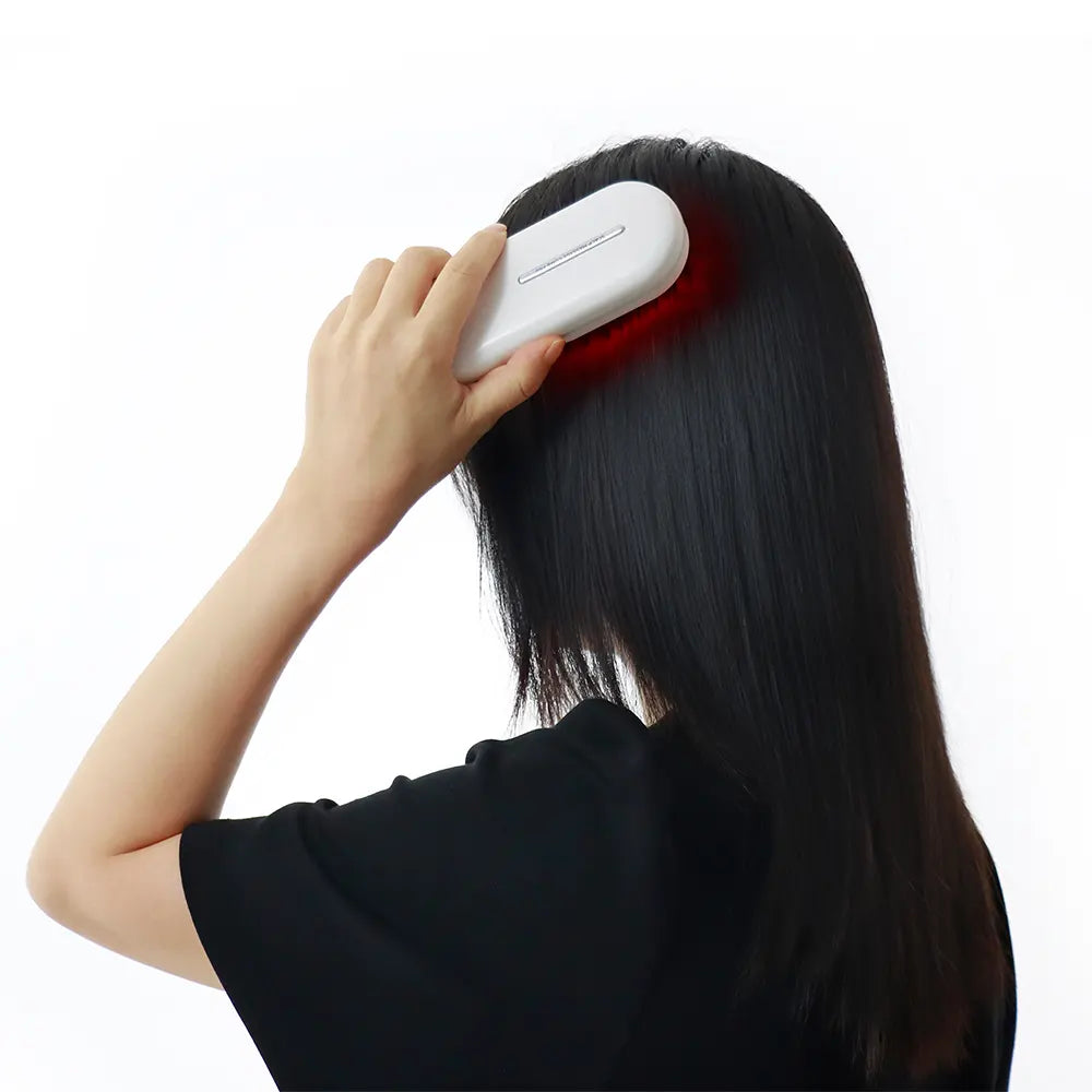 Person using a white electronic hair comb on dark hair against a white background