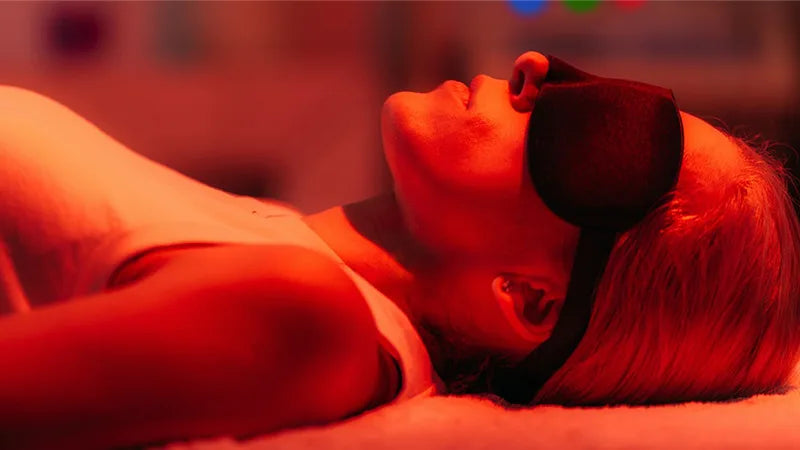 Person lying down with a sleep mask on, bathed in red light.