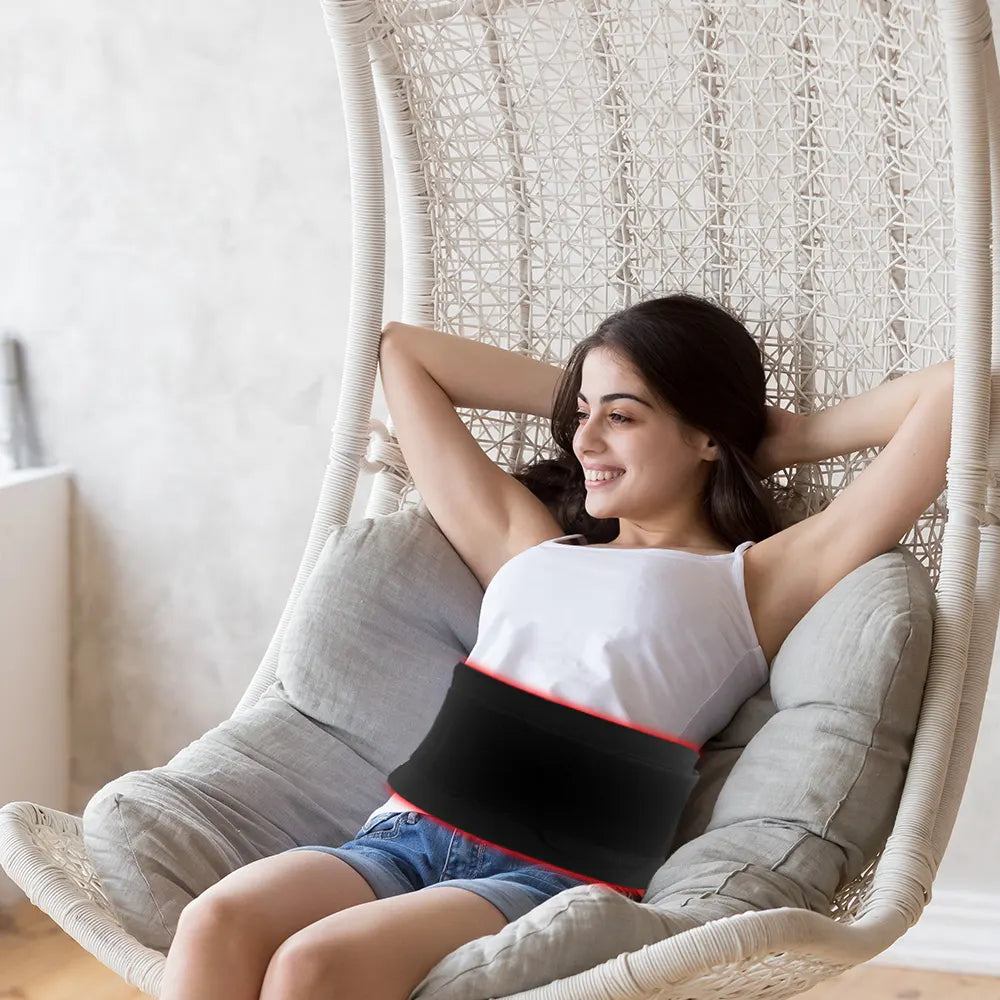 Woman wearing a red infrared light therapy Pad sitting in a wicker chair.