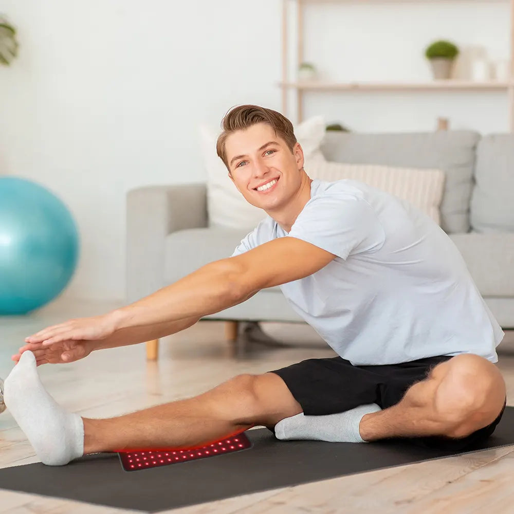 Man stretching on a red infrared light therapy pad in a living room with exercise ball and couch in the background