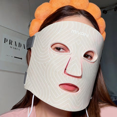 Person wearing a LED face mask with visible branding indoors.
