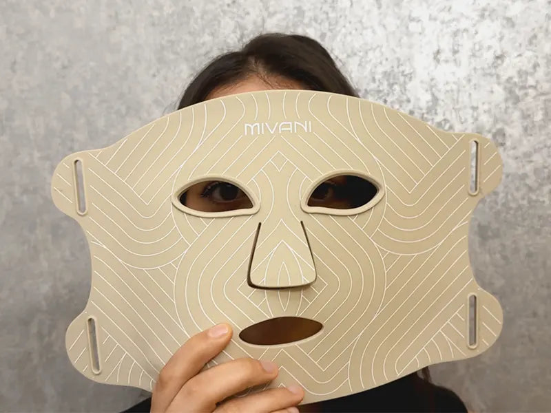 Person holding a beige therapy face mask with 'MIVANI' branding against a gray background