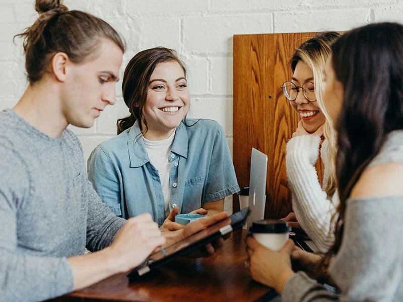 Group of four friends sitting around a table, smiling and interacting.