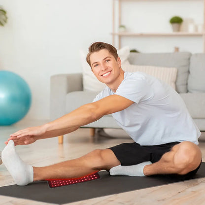 Man stretching on a red infrared light therapy pad in a living room with exercise ball and couch in the background