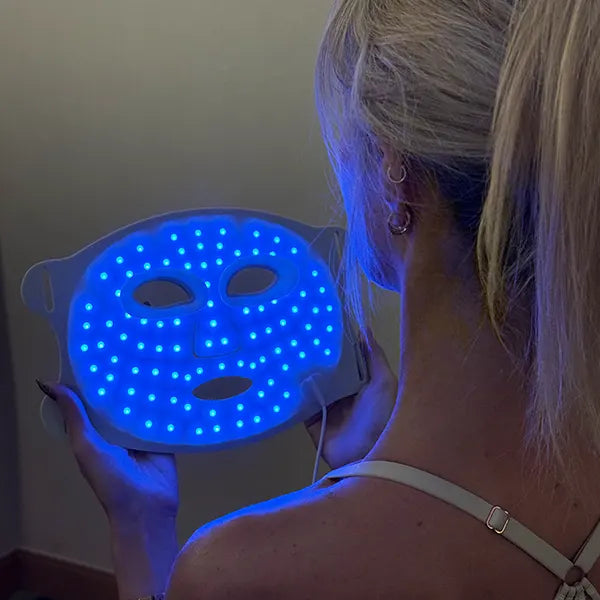 Person holding a blue LED therapy face mask against a neutral background
