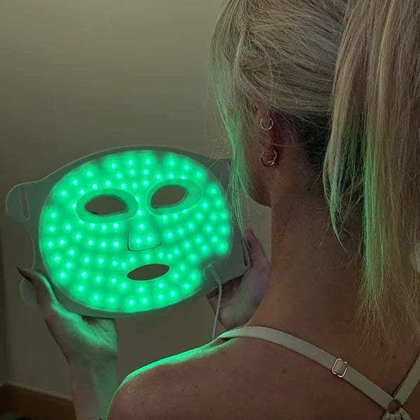 Person holding a green LED therapy face mask against a neutral background