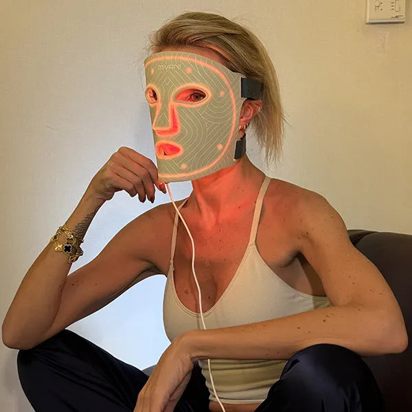 Person wearing an orange LED Light therapy face mask sitting on a couch with a blurred face