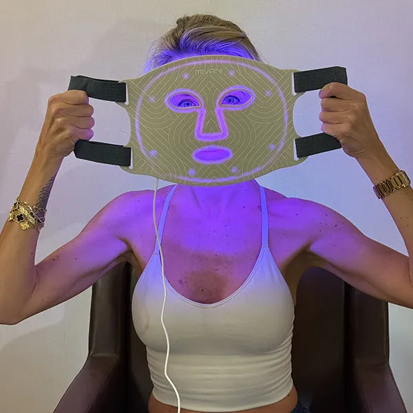 Person holding a therapy face mask with purple LED lights on a plain background