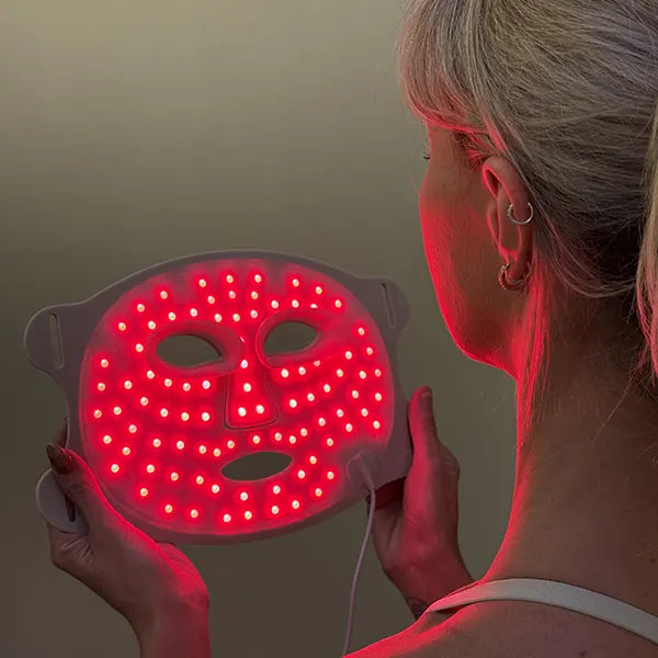 Person holding a red LED therapy face mask against a neutral background